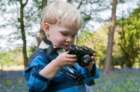 孩子拿着LUMIX相机，在一片蓝铃木中玩耍。