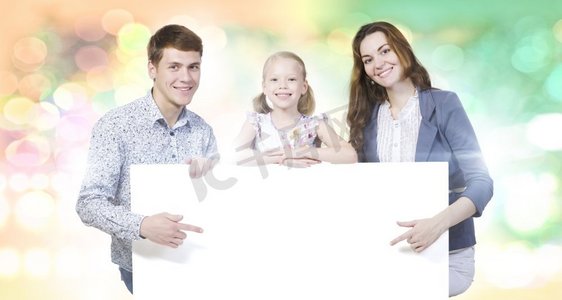 快乐家庭海报摄影照片_年轻的家庭。幸福的一家三口举着白色的空白横幅。文本位置