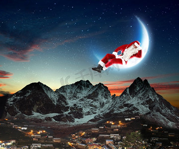 圣诞老人坐在月球上的照片。圣诞老人坐在月亮上，下面是一座城市和一座山