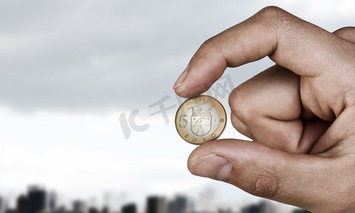 观看摄影照片_手指间夹着5欧元硬币。近距离观看男性手采取与手指欧元硬币