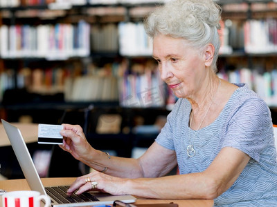 一位拿着卡片、拿着笔记本电脑工作的老妇人。网上购物