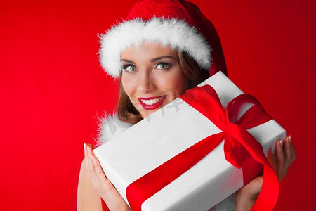 戴着圣诞老人帽子的女人带着礼物。戴着圣诞帽的漂亮年轻女子手持礼品盒庆祝圣诞节