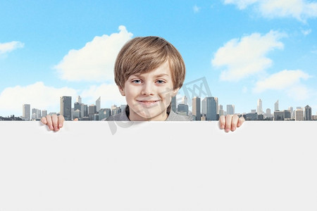 小男孩拿摄影照片_拿着一块空白广告牌的男孩。一个小男孩拿着一块空白的白色广告牌