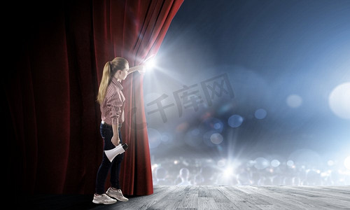 拿喇叭说话摄影照片_拿着扩音器的女孩年轻的女孩在舞台上与扩音器开放红色窗帘