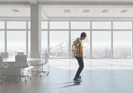 男孩骑滑板。活跃的家伙在办公室内部玩滑板。混合介质