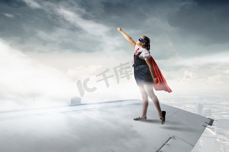 超级小英雄摄影照片_小超级英雄。强大的超级英雄小女孩站在飞行的飞机机翼上