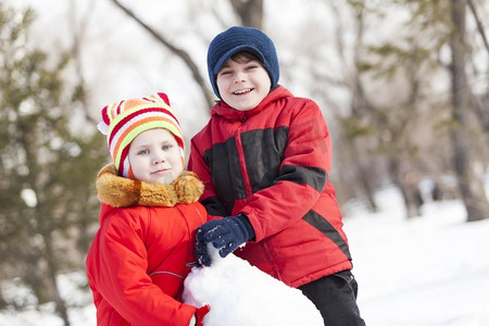 可爱的男孩和女孩在冬季公园堆雪人。冬季活动小游戏