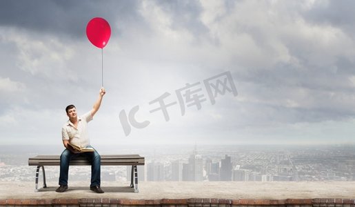 看书距离摄影照片_胖子胖子坐在长凳上手里拿着书和气球