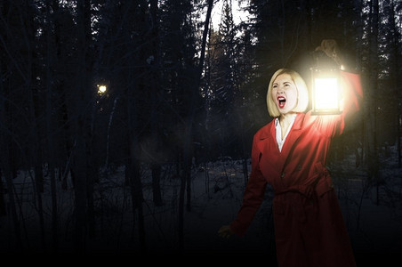 元宵节小报模板摄影照片_迷失的女人年轻的金发女郎在红色斗篷与灯笼在夜间森林