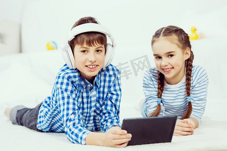可爱的孩子在平板电脑上玩游戏。男孩和女孩躺在地板上使用平板电脑