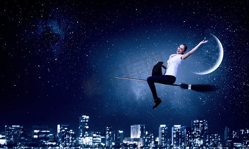 万圣节免费摄影照片_穿着休闲的少女骑着扫帚在高空飞翔。扫帚上的女孩