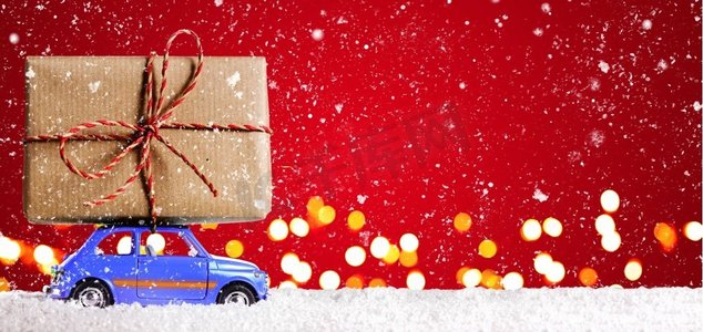 带有圣诞礼物的复古玩具车。蓝色复古玩具车在节日红色背景下递送圣诞或新年礼物
