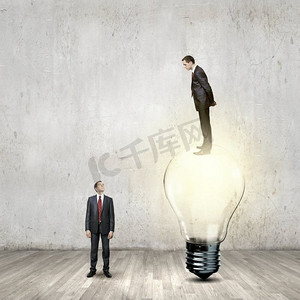 升级换代摄影照片_商业上的进步。一位商人站在灯泡上，俯视着同事