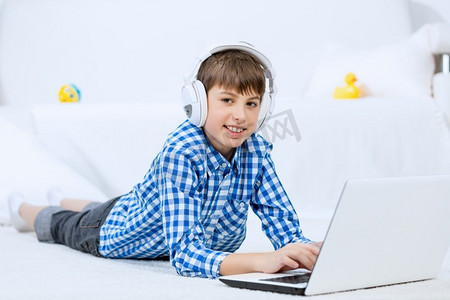 享受休闲时光的孩子。学龄儿童躺在地上通过耳机听笔记本电脑上的音乐