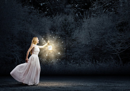 带灯笼的女人。年轻女子在白色长裙走在夜间木材
