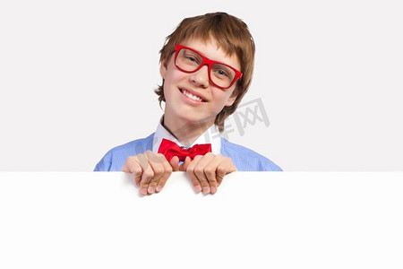 红白色海报摄影照片_戴红眼镜的男孩拿着白色方块。小男孩笑着抱着白色方块的形象。刊登广告的地点