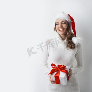 戴着圣诞帽的女孩拿着礼品盒。戴着圣诞老人帽子的可爱的笑女孩拿着礼盒