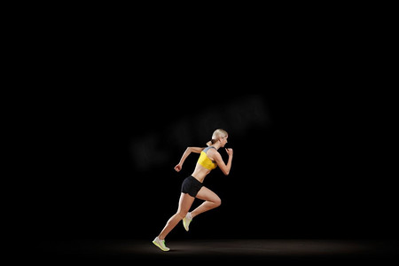 全速前进。年轻女子运动员跑得快在黑暗的背景 