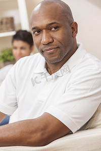 一个英俊的非裔美国男子坐在家里沉思着，他的女朋友或妻子在他身后