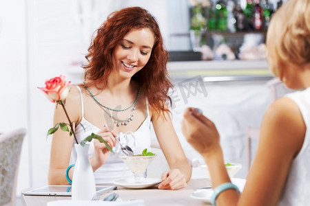 咖啡馆里的可爱女孩。两个年轻漂亮的女人坐在咖啡馆里吃着甜点