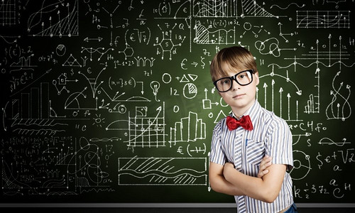 聪明的小学生。戴着红眼镜的天才男孩在黑板上写着公式