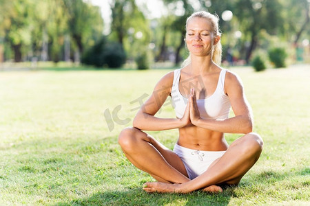 瑜伽练习。身着白衣的年轻女子以莲花的姿势坐在草地上