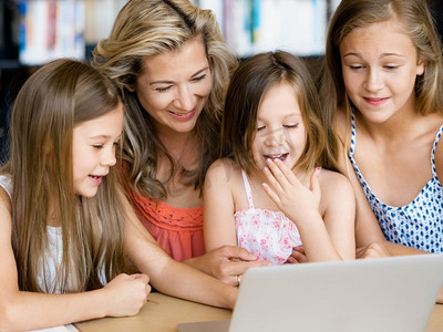 小女孩和她们的妈妈在图书馆里拿着笔记本电脑。图书馆里的科技和乐趣