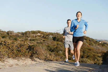 跑步情侣摄影照片_运动跑步者在海滩上慢跑，和她的伴侣一起锻炼。健康的女健身模特和她的伴侣沿着海洋慢跑