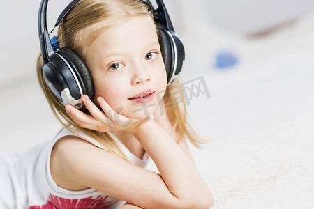倾听孩子的声音摄影照片_戴着耳机享受音乐的可爱女孩。我喜欢听音乐
