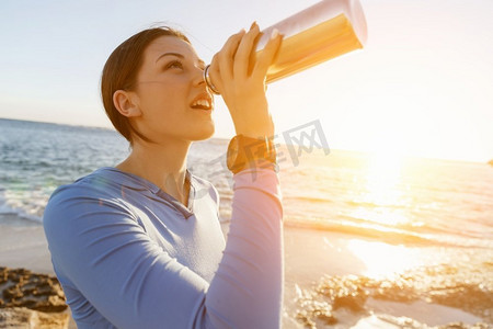 出水素果摄影照片_女人在海滩上喝水。年轻女子饮用水后行使在海滩上