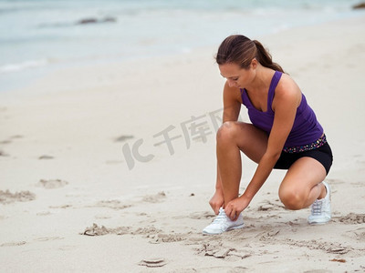 活力四射的年轻女子在海边系鞋带