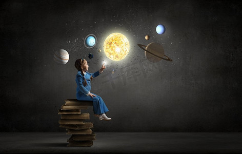 小女孩探索太空。小女孩坐在一堆书上，触摸着地球