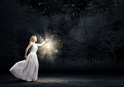 带灯笼的女人。年轻女子在白色长裙走在夜间木材