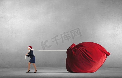 背着大麻袋的圣诞老人。戴着圣诞帽的女人拉着巨大的红色礼物袋