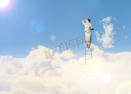 站在梯子上的女商人。站在梯子上的女商人在多云的背景下眺望远方