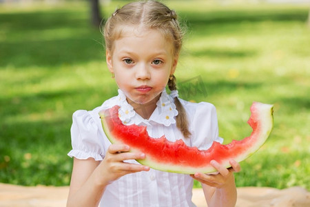 吃西瓜的女孩摄影照片_吃西瓜的女孩。公园里的可爱女孩吃着多汁的西瓜