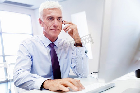 一位商人坐在办公室的电脑前打电话。保持联系和联系