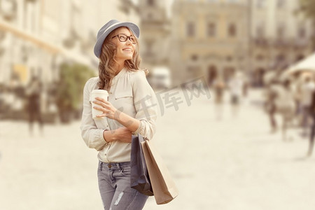 快乐的年轻时尚女性，提着购物袋，在购物后喝咖啡，拿着外卖咖啡，在城市背景下。