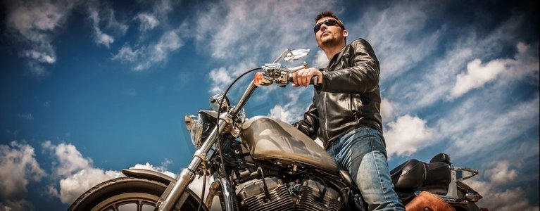 骑摩托的男人摄影照片_一名骑自行车的男子穿着皮夹克，戴着墨镜坐在他的摩托车上。