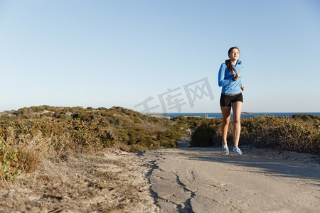 运动跑步者在海滩上慢跑锻炼。健康的女性健身模特沿着海洋慢跑