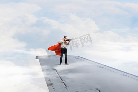 他飞得很高。站在机翼边上拉小提琴的超人