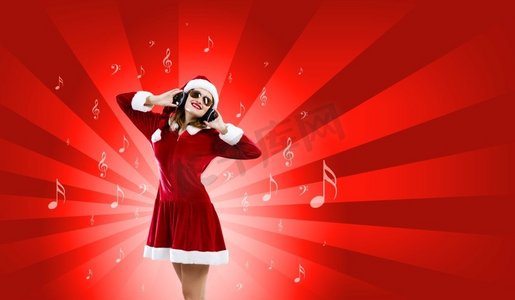 庆祝新年。年轻有吸引力的圣诞老人女孩听音乐在耳机
