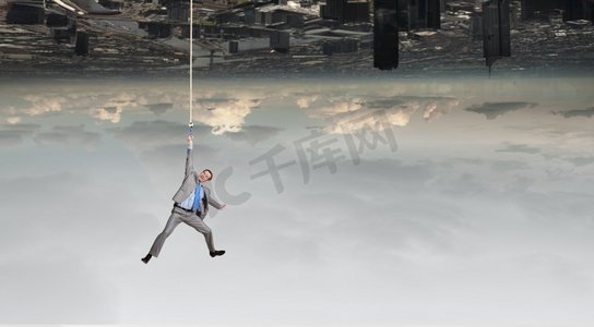 一位年轻的商人吊在城市上空的绳子上。一名男子挂在绳子上