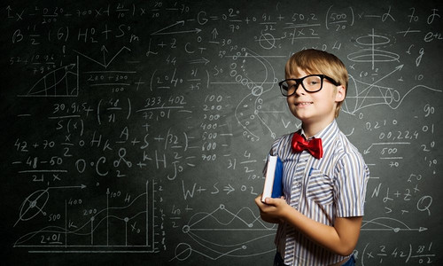 聪明的小学生。戴着红眼镜的天才男孩在黑板上写着公式