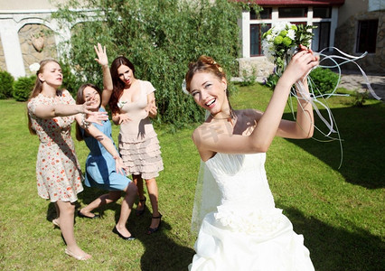 粉色婚纱摄影照片_身着白色婚纱的年轻新娘向伴娘抛出一束鲜花