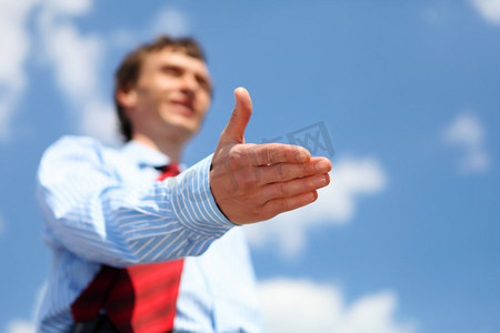 一位穿着蓝色衬衫，打着红色领带的年轻商人伸出手握手