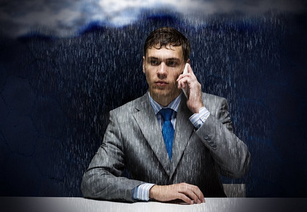商业挑战。雨中沮丧的年轻商人打着手机