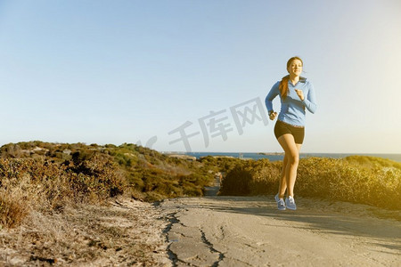 模特跑步摄影照片_运动跑步者在海滩上慢跑锻炼。健康的女性健身模特沿着海洋慢跑