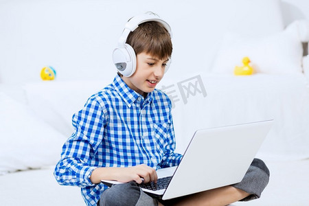 孩子享受休闲时光。学龄男孩听音乐从笔记本电脑通过耳机，而坐在地板上
