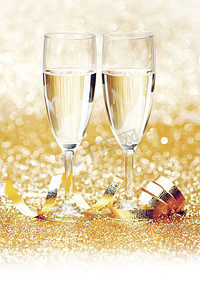 邀请函香槟色摄影照片_酒杯上的香槟和金色的丝带在白色上闪闪发光